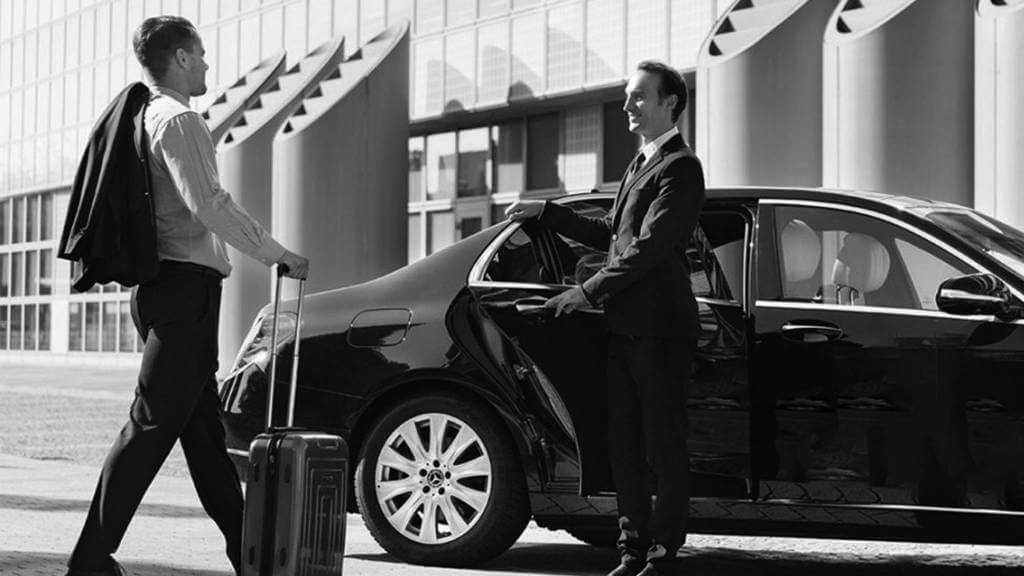 Two business men standing next to a black car.