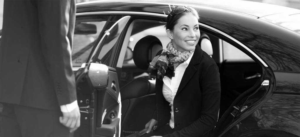 A black and white photo of a woman getting out of a car.