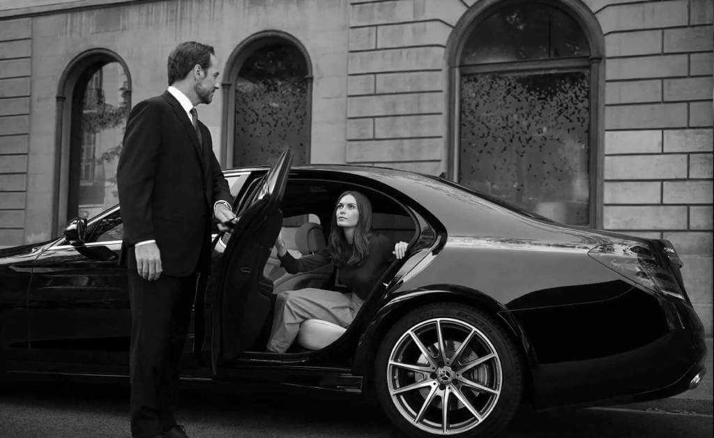 A black and white photo of a man and woman getting into a mercedes benz.
