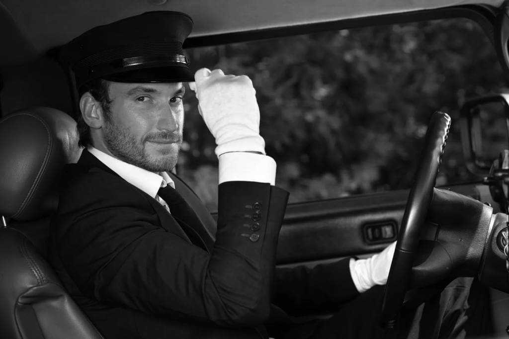 A man in a suit sitting in the driver's seat of a car.