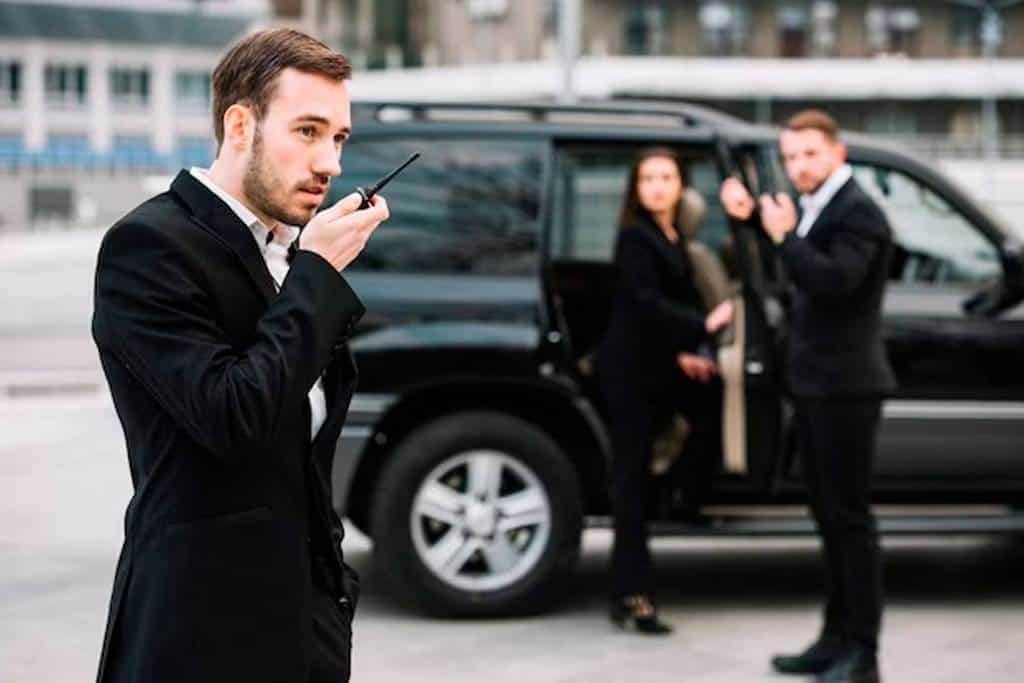 A man and woman in suits conversing on a cell phone while traveling in a New York car service.