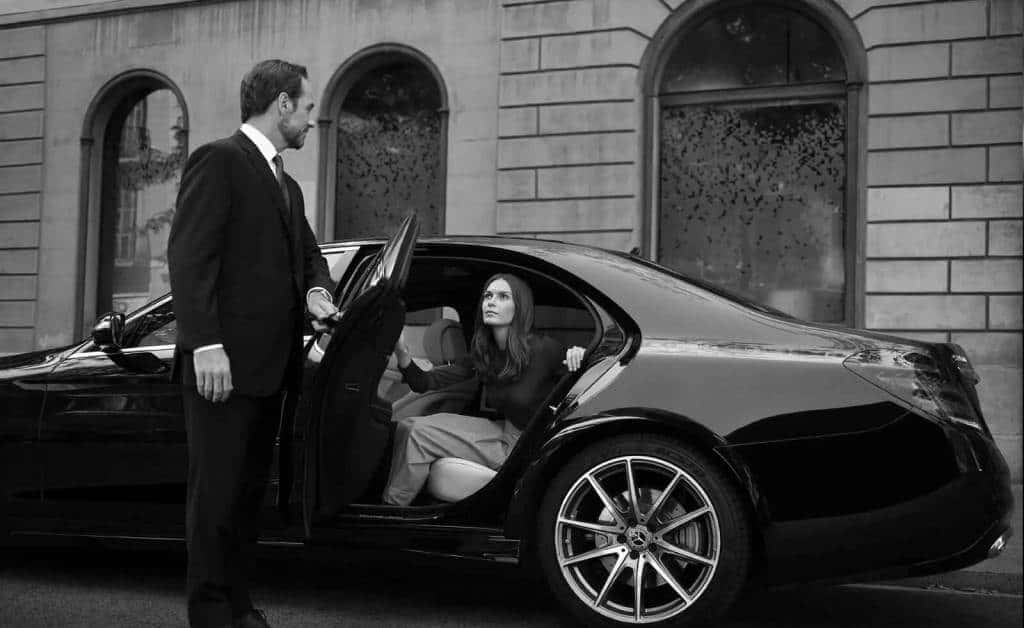 A black and white photo of a Sonic D Limousine Chauffer and woman getting into a Luxury Sonic D Limousine mercedes benz.