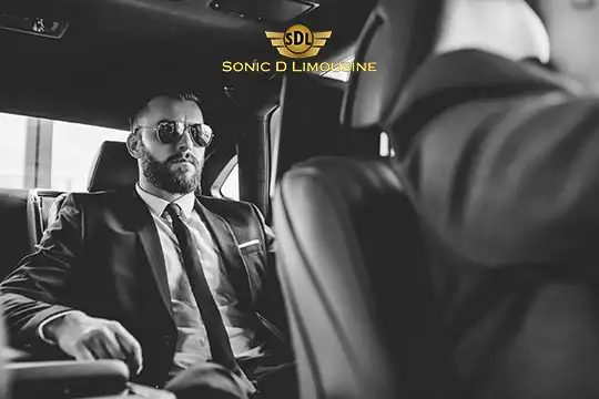 Sonic D Limousine Worldwide Voted Most Reliable Airport Transportation Provider! A man wearing sunglasses and a suit sits in the backseat of a limousine. The logo "Sonic D Limousine" is visible above him, emphasizing their luxury airport transportation services. Sonic D Limousine Worldwide your luxury Airport Transportation