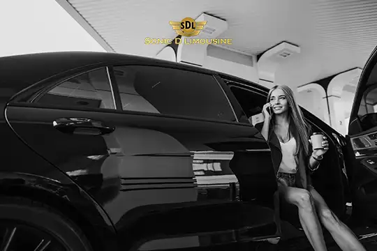 Sonic D Limousine Worldwide Voted Most Reliable Airport Transportation Provider! A woman holding a cup and smiling steps out of the backseat of a black limousine. The "Sonic D Limousine Luxury Airport Transportation" sign is visible in the background. Sonic D Limousine Worldwide your luxury Airport Transportation