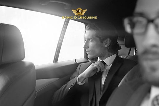 Sonic D Limousine Worldwide Voted Most Reliable Airport Transportation Provider! Two men in suits sit in the backseat of a car. One man adjusts his tie while looking out the window, reflecting on their journey with Sonic D Limousine Luxury Airport Transportation. The logo "Sonic D Limousine" is visible above them, underscoring their first-class experience. Sonic D Limousine Worldwide your luxury Airport Transportation