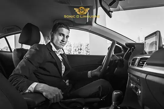 Sonic D Limousine Worldwide Voted Most Reliable Airport Transportation Provider! A man in a suit sits in the driver's seat of a car, looking at the camera and smiling. The car's interior exudes elegance, and "Sonic D Limousine Luxury Airport Transportation" is branded above. Sonic D Limousine Worldwide your luxury Airport Transportation