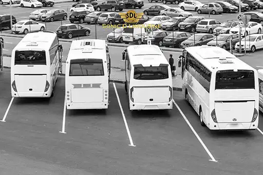 Sonic D Limousine Worldwide Voted Most Reliable Airport Transportation Provider! Four parked buses are lined up side by side in a parking area. A large number of cars fill the background. The words "Sonic Chauffeur Logistics" are visible on a banner, highlighting their role in Sonic D Limousine Luxury Airport Transportation. Sonic D Limousine Worldwide your luxury Airport Transportation