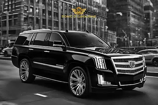 Sonic D Limousine Worldwide Voted Most Reliable Airport Transportation Provider! A black Sonic D luxury SUV with a logo on the front cruises through a city street, surrounded by tall buildings, epitomizing Limousine Luxury Airport Transportation. Sonic D Limousine Worldwide your luxury Airport Transportation