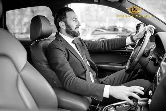 Sonic D Limousine Worldwide Voted Most Reliable Airport Transportation Provider! Black and white image of a man in a suit driving a car, with a logo of "Sonic D Limousine Luxury Airport Transportation" in the top right corner. Sonic D Limousine Worldwide your luxury Airport Transportation