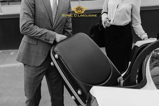 Sonic D Limousine Worldwide Voted Most Reliable Airport Transportation Provider! A person in a suit loads a suitcase into the trunk of a Sonic D Limousine while another individual stands nearby, holding a handbag. Sonic D Limousine Worldwide your luxury Airport Transportation