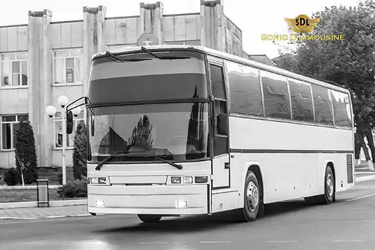 Sonic D Limousine Worldwide Voted Most Reliable Airport Transportation Provider! A white luxury tour bus from Sonic D Limousine, renowned for its premium airport transportation services, is parked on a street in front of a building. Sonic D Limousine Worldwide your luxury Airport Transportation