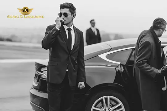 Sonic D Limousine Worldwide Voted Most Reliable Airport Transportation Provider! Three men dressed formally stand near a luxury car with the logo "SDL Sonic D Limousine" visible in the top left corner. Two men are near the car, discussing Sonic D Limousine's premier service, while the third is in the background, ensuring seamless luxury airport transportation. Sonic D Limousine Worldwide your luxury Airport Transportation